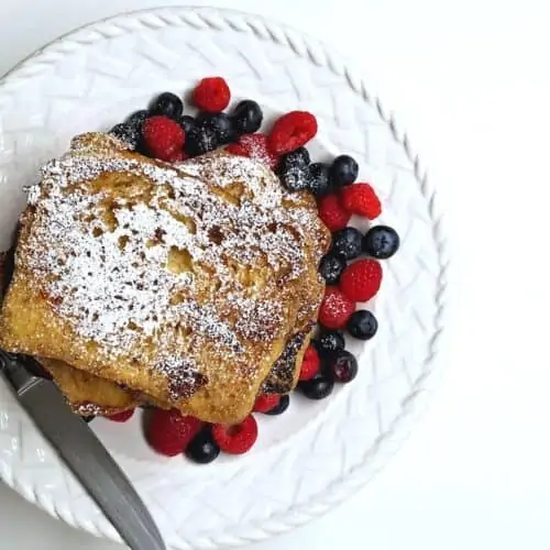Plate of homemade French toast with mixed berries and powdered sugar.