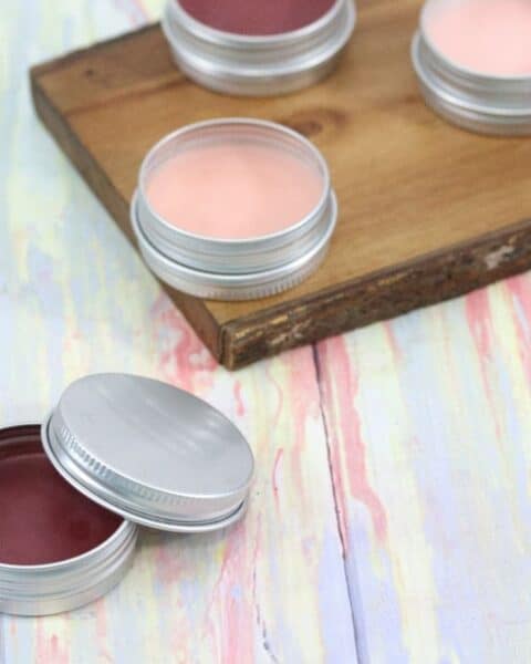 Homemade tinted lip balm on wooden board and table.