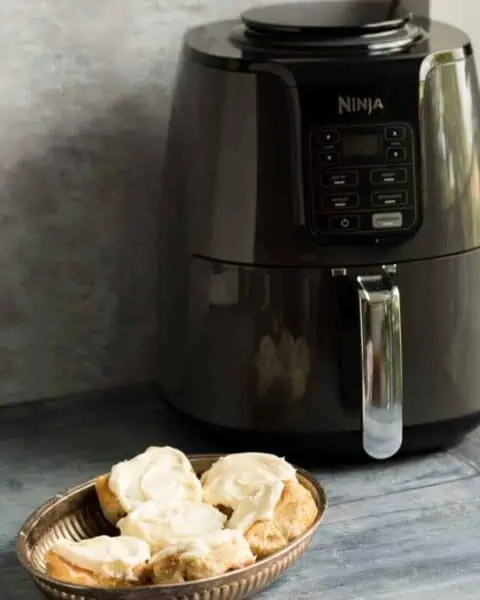 A Ninja airfryer on a kitchen countertop with a basket of cinnamon rolls.