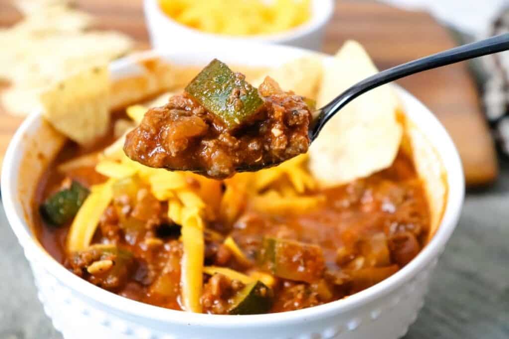 A bowl of ground venison chili with shredded cheese and tortilla chips.