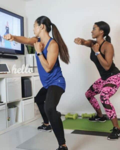 Two women working out together with weights and yoga mat with the Healthy U TV.