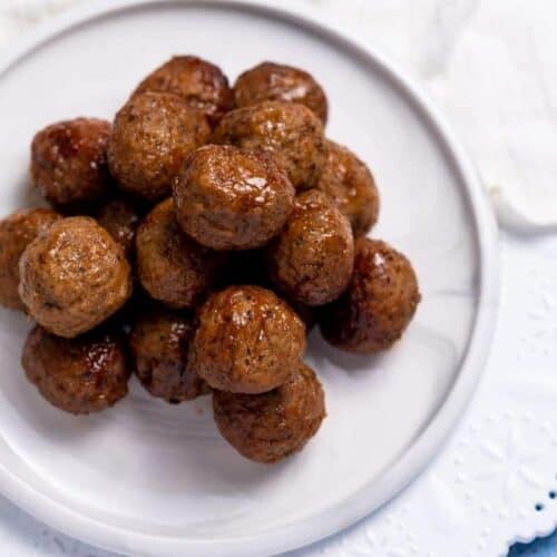 Close up of grape jelly meatballs on a white plate.