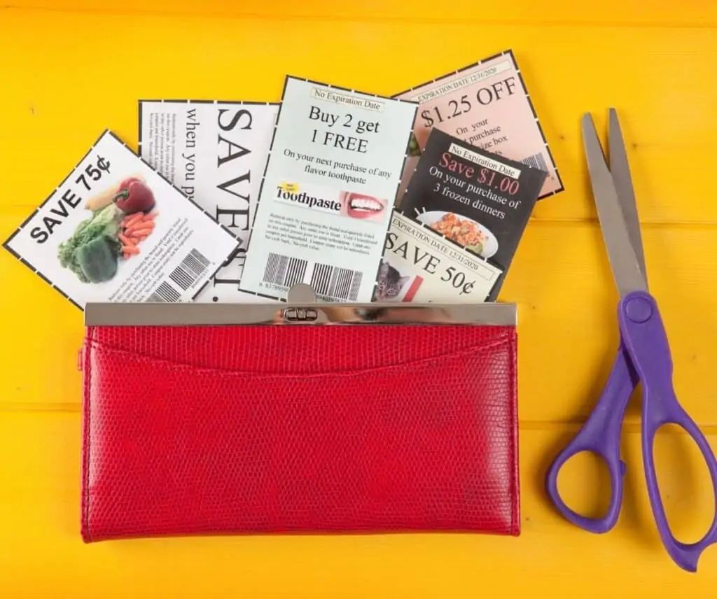 A red purse with cut coupons in the bag next to a pair of scissors.