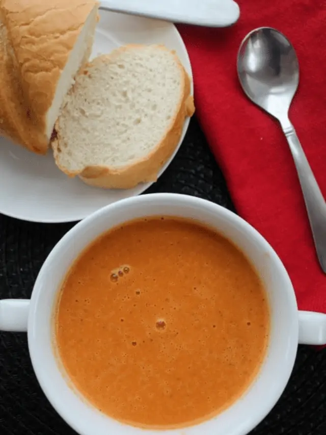 Crock Pot Creamy Tomato Soup in a white bowl next to a slice of white bread.