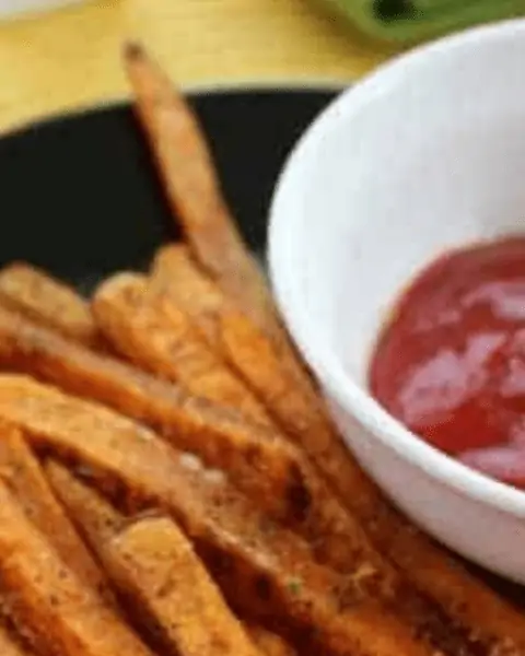 Sweet Potato Fries on a black plate with a bowl of ketchup.