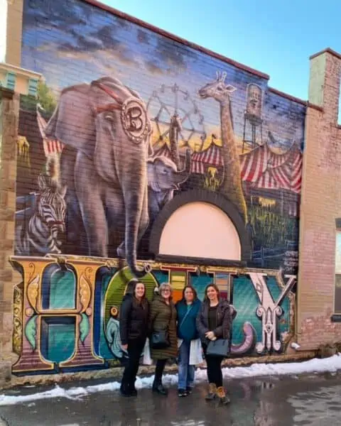 A group of people standing outside a brick building with artwork on the building.
