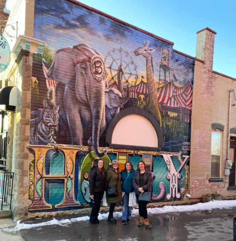 A group of people standing outside a brick building with artwork on the building.