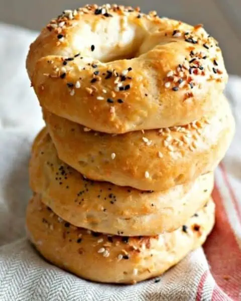 A stack of homemade bagels with everything seeds seasoning on top of each bagel.