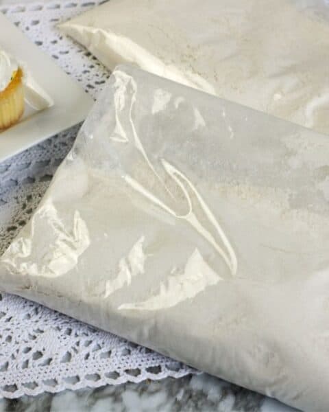 Dry ingredients to make a yellow cake mix in a bag next to a plate of yellow cake mix cupcakes with frosting.