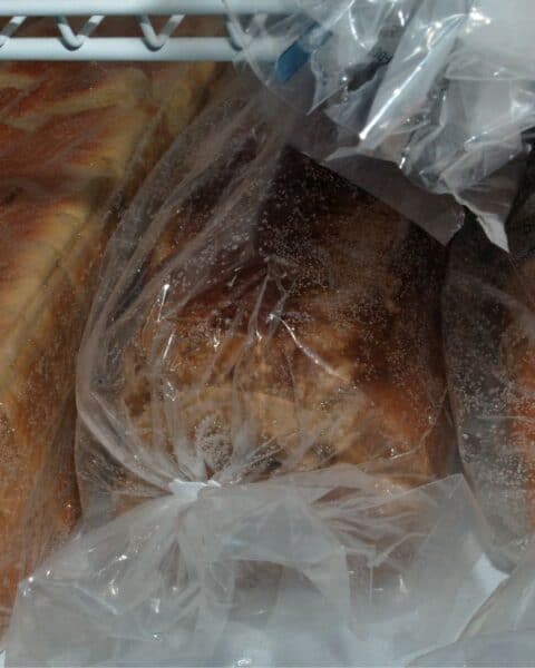 Several loaves of bread in wrappers next to each other in the freezer.