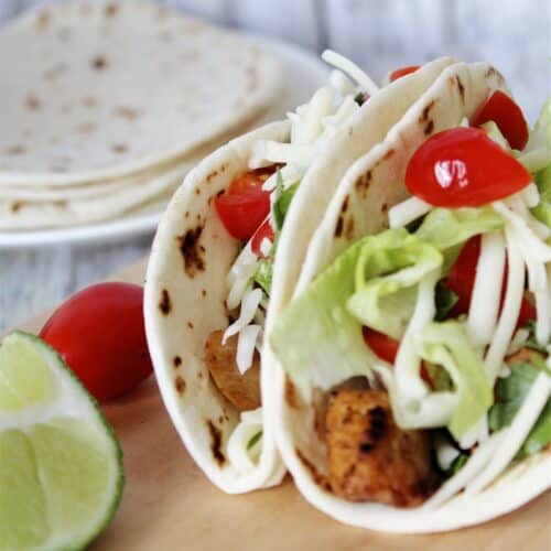 Crispy chicken tacos with a side of lime and tomatoes.