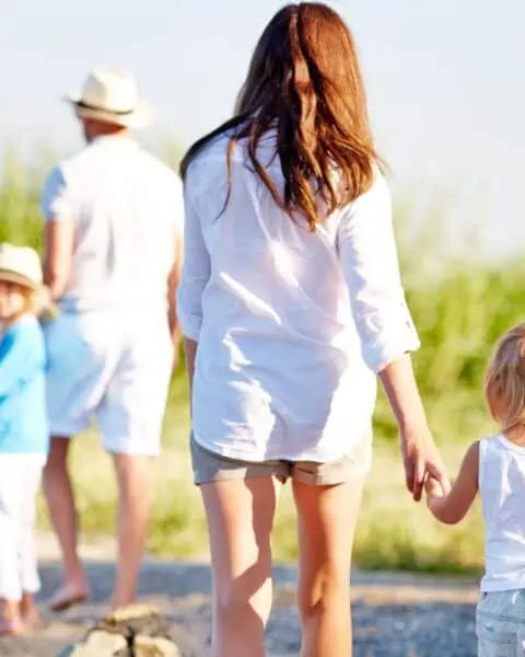 A woman holding a small child's hand as their family goes on a walk together.