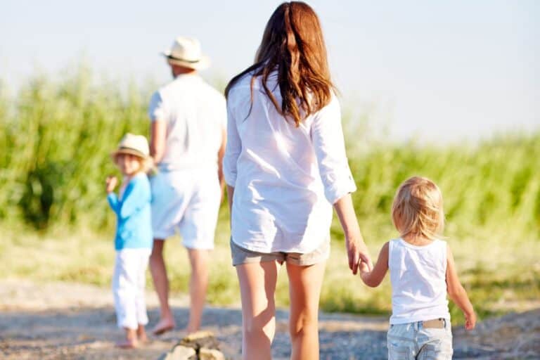 A woman holding a small child's hand as their family goes on a walk together.