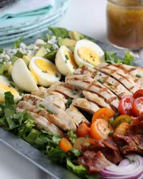 Closeup of chicken cobb salad on a serving tray with a side of homemade dressing.