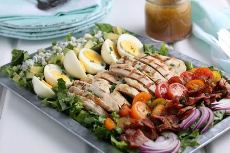 Closeup of chicken cobb salad on a serving tray with a side of homemade dressing.
