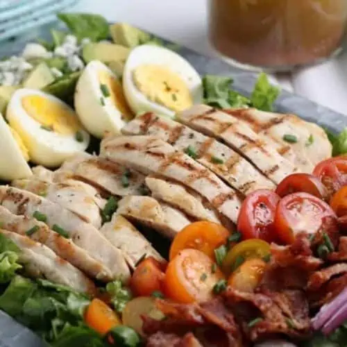 Closeup of chicken cobb salad on a serving tray with a side of homemade dressing.