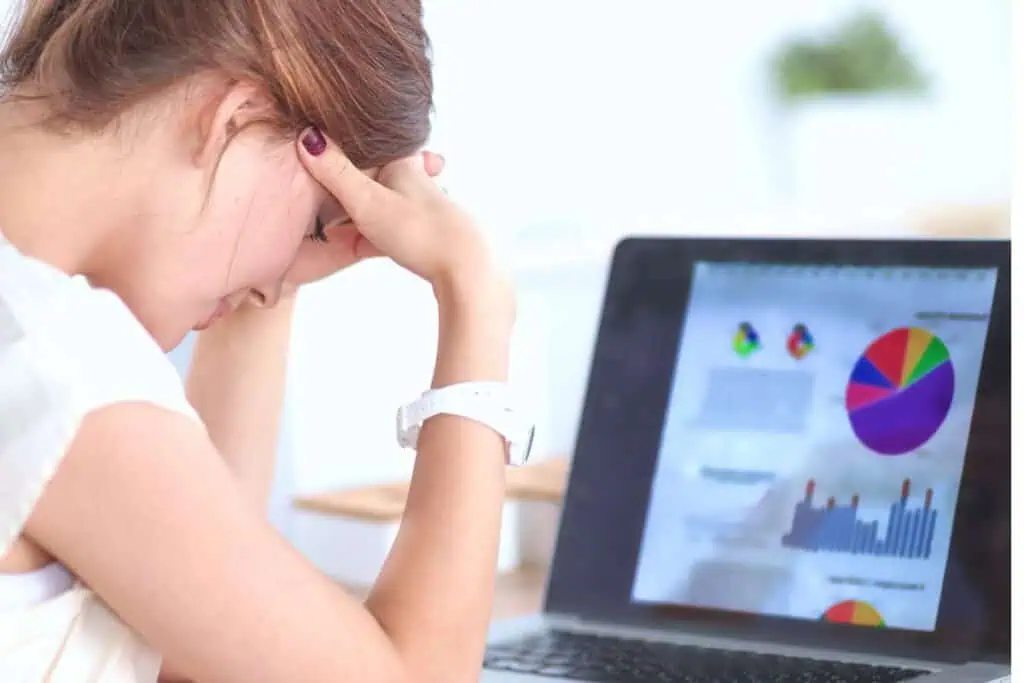 A person with a watch on their wrist sits with their head in their hands, trying to choose the right budget method while looking at a laptop displaying colorful graphs and charts.