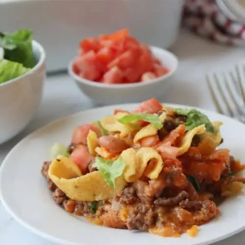 A plate full of walking tacos with Fritos and toppings.