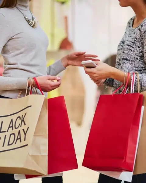 Two women carrying shopping bags with Black Friday on the bags.