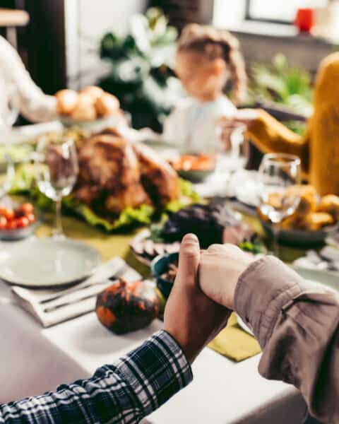 Family sitting around the Thanksgiving table holding hands and saying prayers.