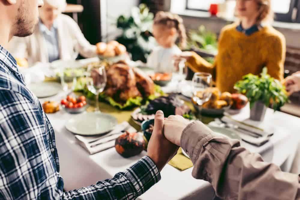 Family sitting around the Thanksgiving table holding hands and saying prayers.