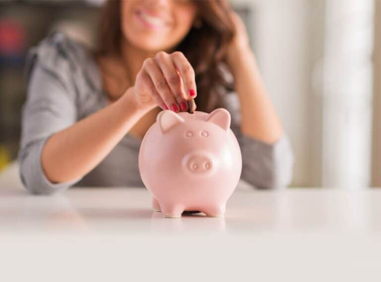 A woman putting money in a piggy bank.