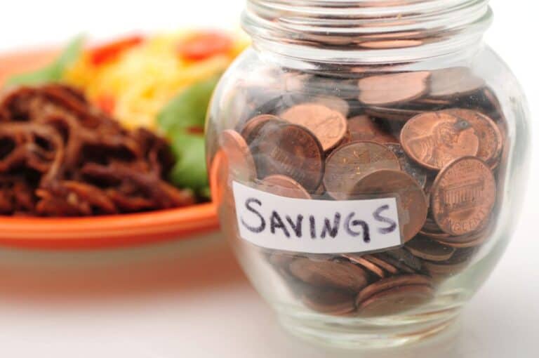 A small glass jar filled with pennies. The jar has a tapped label that reads, "savings."