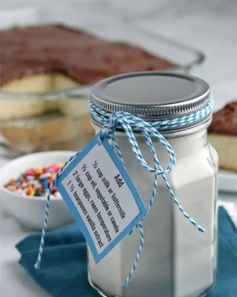 A small mason jar of dry ingredients for a homemade yellow cake mix. The jar is wrapped with a blue and white ribbon.