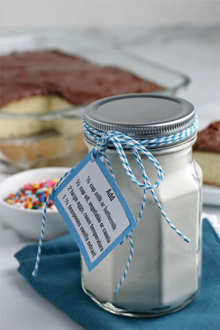 A small mason jar of dry ingredients for a homemade yellow cake mix. The jar is wrapped with a blue and white ribbon.