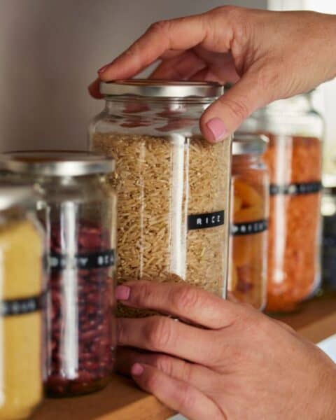 A person is preserving food for long term storage by placing it into jars on a shelf.