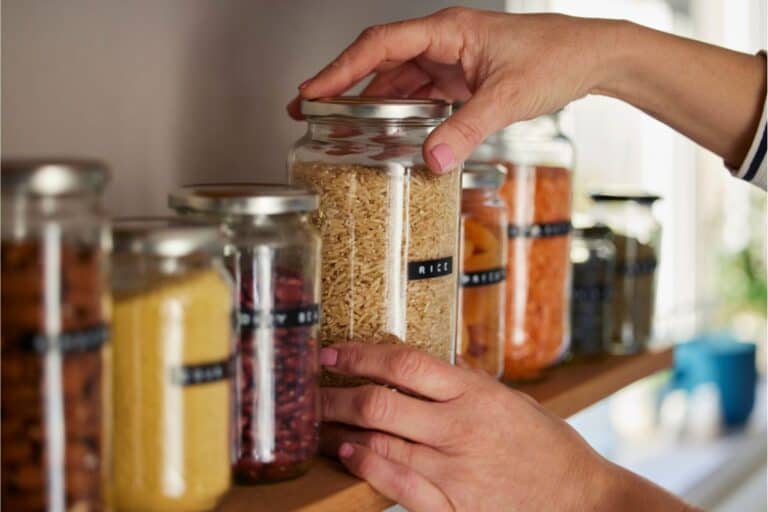 A person is preserving food for long term storage by placing it into jars on a shelf.