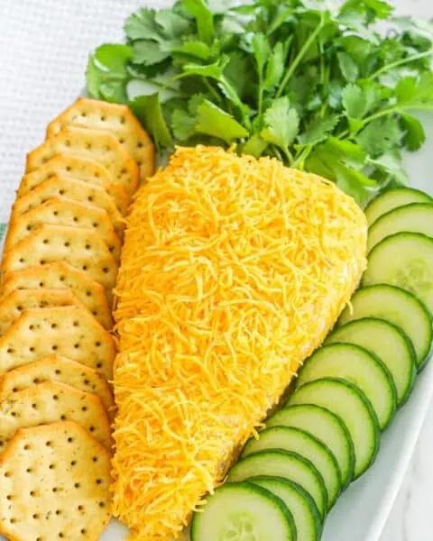 Easy carrot cheese dip served with crackers and cucumbers on a white plate.