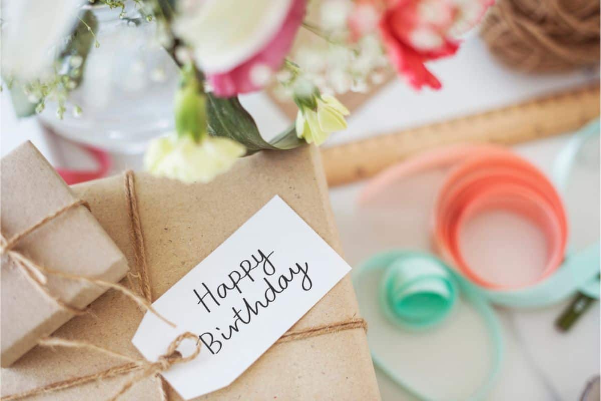 A brown paper package with a "Happy Birthday" tag, surrounded by flowers and colored ribbons, promises delightful birthday freebies within its charming wrap.