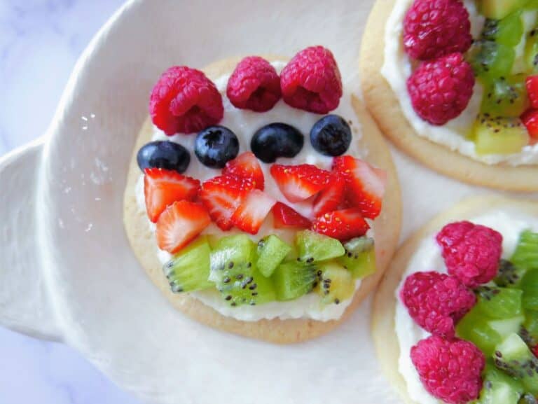 A plate of mini fruit pizzas topped with whipped cream.