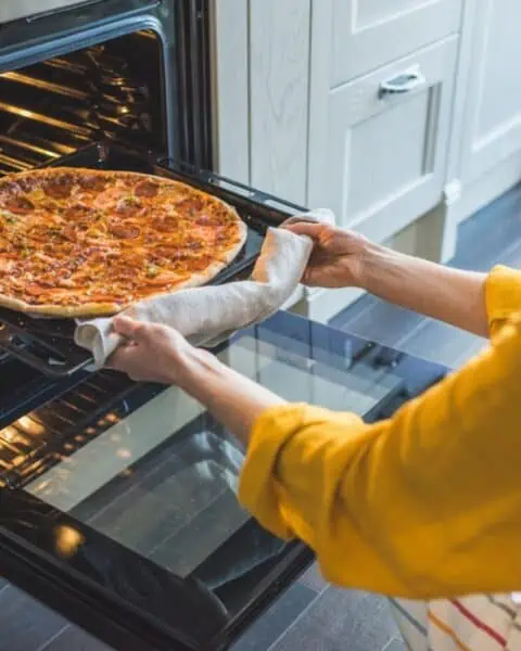 A woman is using an easy pizza dough recipe to put a pizza in the oven.