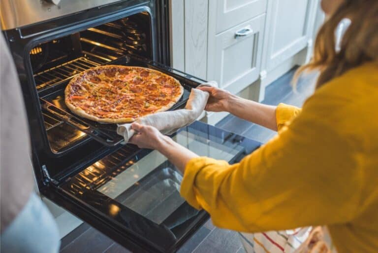 A woman is using an easy pizza dough recipe to put a pizza in the oven.