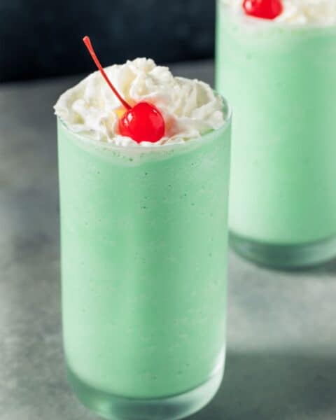 Shamrock shake recipe featuring two green drinks topped with whipped cream and a cherry.
