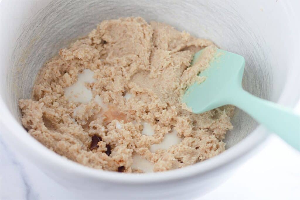 A bowl of edible chocolate chip cookie dough with a green spatula in it.