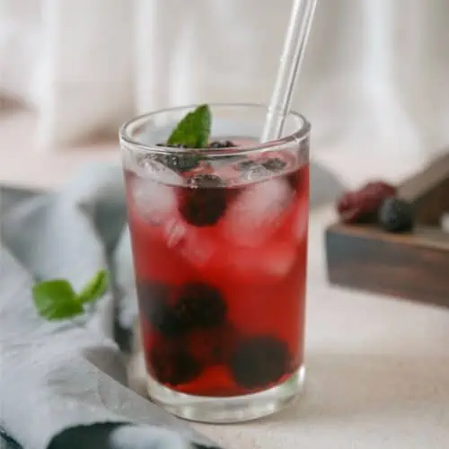 A refreshing Very Berry Hibiscus iced tea with a blackberry twist, garnished with a straw.