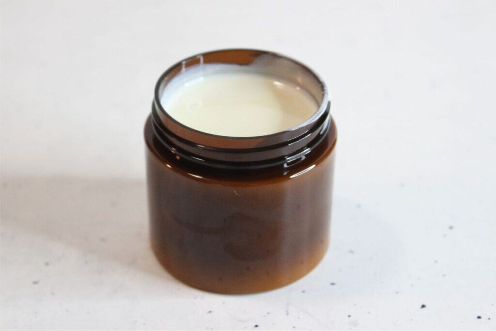 An open brown jar filled with a white cream, placed on a plain light-colored surface, showcases a natural sunscreen perfect for daily skincare.