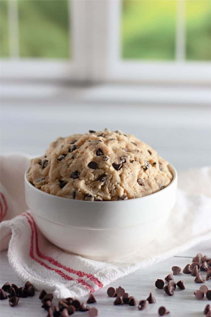 A bowl of edible chocolate chip cookie dough on a white table.
