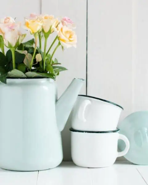 An old-fashioned teapot and mug adorned with flowers on a rustic wooden table.