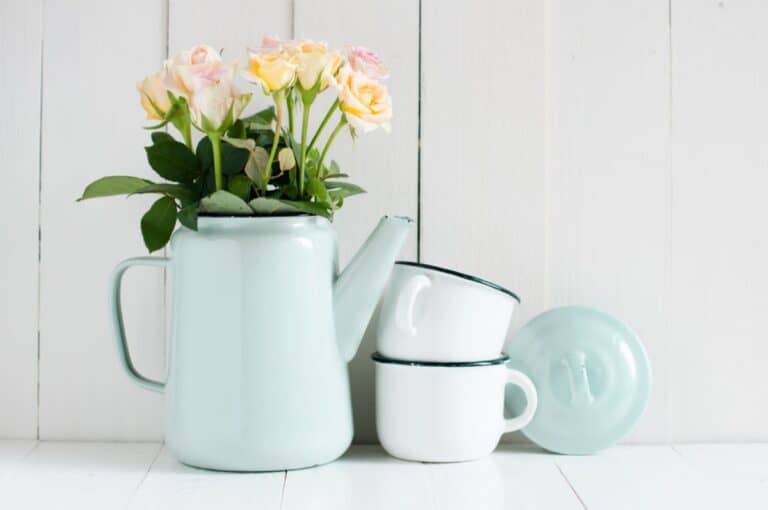 An old-fashioned teapot and mug adorned with flowers on a rustic wooden table.