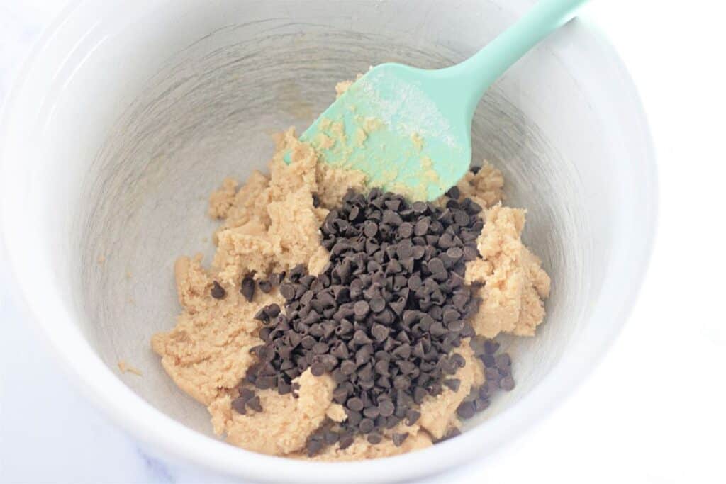 Edible chocolate chip cookie dough being prepared with a green spatula.