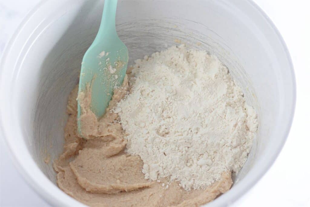 A bowl filled with edible chocolate chip cookie dough and a green spoon.