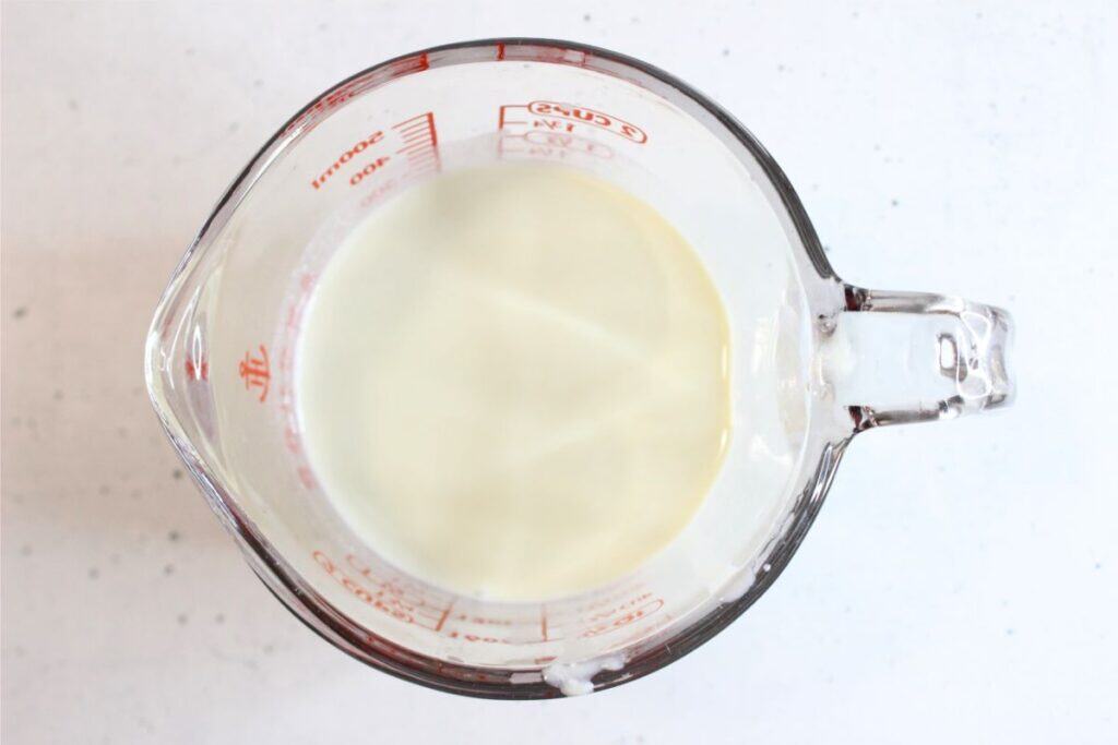 A glass measuring cup filled with milk, viewed from above on a white surface—milk is known by some for its natural sunscreen properties.