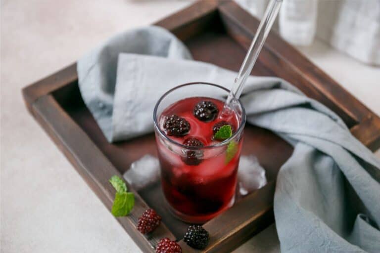 A Very Berry Hibiscus Refresher with blackberries and mint arranged on a wooden tray.