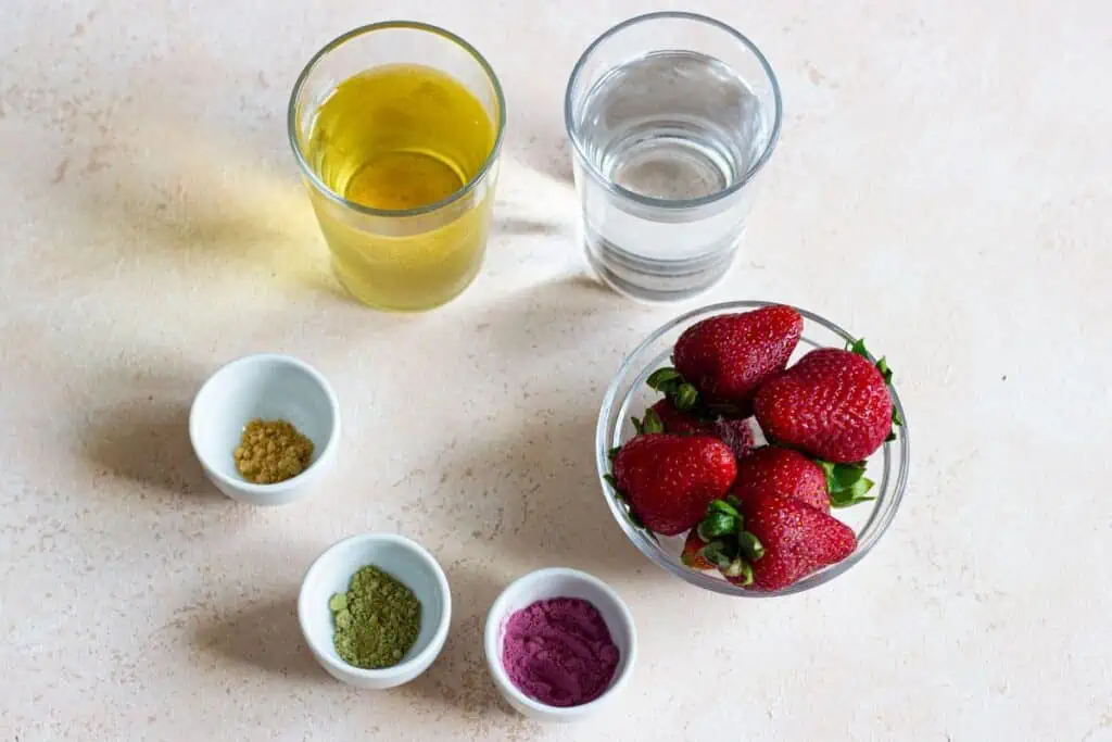 A bowl of strawberries and a glass of water garnished with a Starbucks Strawberry Acai Refresher powder.