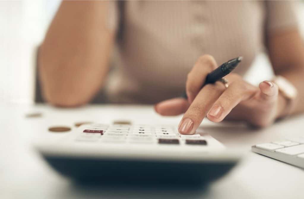 A woman is making household budgeting mistakes while using a calculator on a desk.