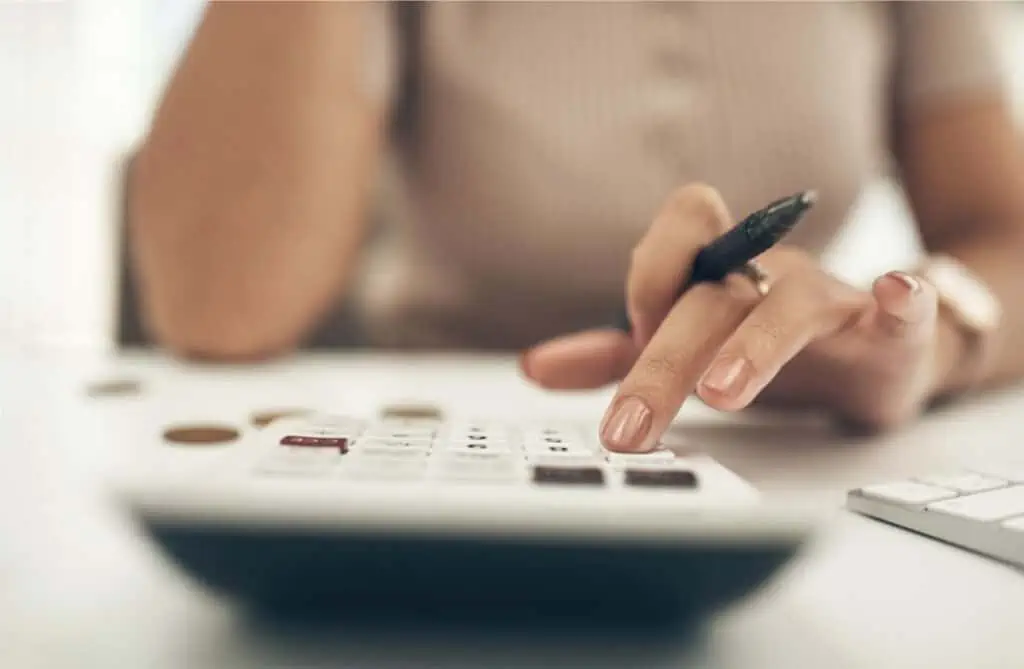 A woman is making household budgeting mistakes while using a calculator on a desk.